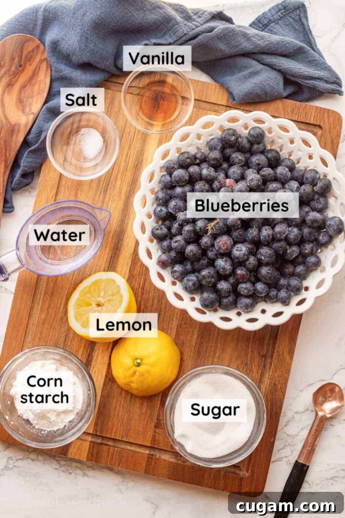 Ingredients for homemade blueberry pie filling labeled in glass dishes on wood cutting board. 