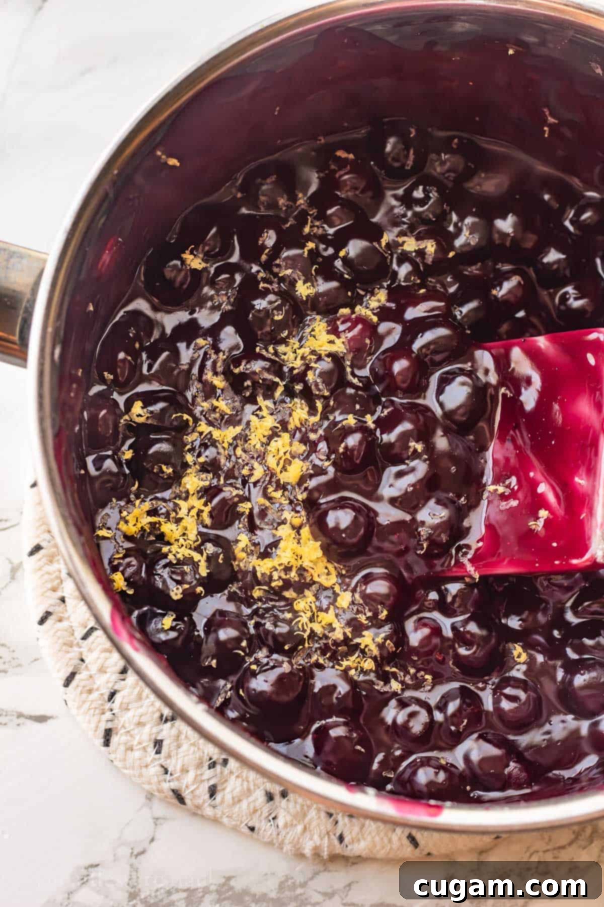 Cooked blueberry pie filling in metal pot with lemon zest.