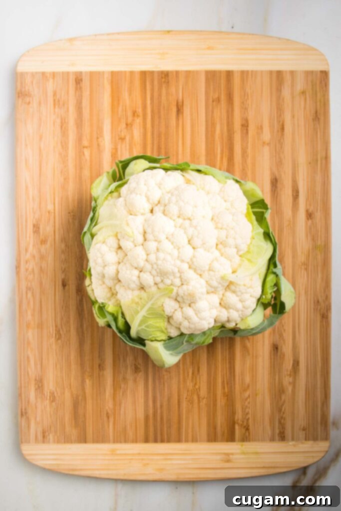 Whole head of cauliflower resting on a bamboo wooden cutting board.