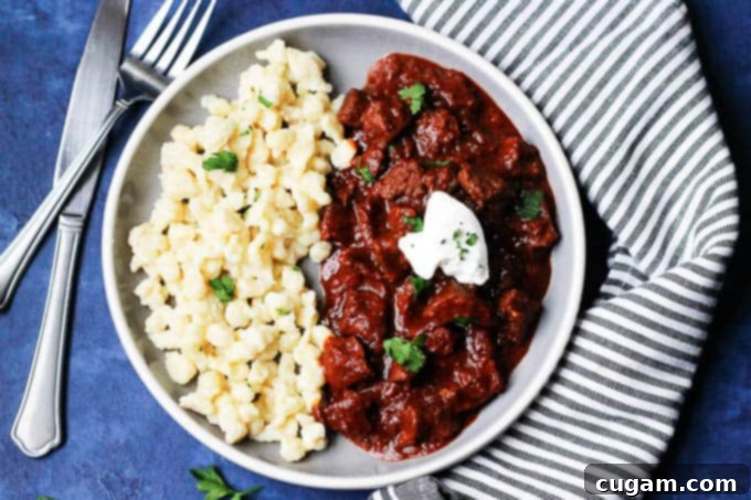 Serving Hungarian Porkolt Goulash with egg noodles and a spoonful of sour cream