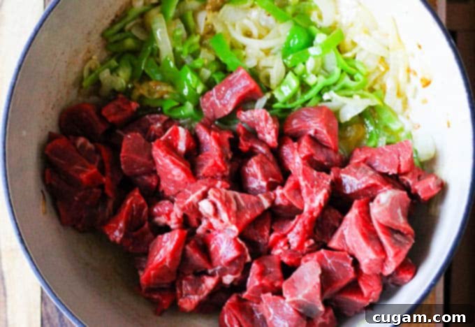Searing small-cubed beef in a pot with onions and peppers