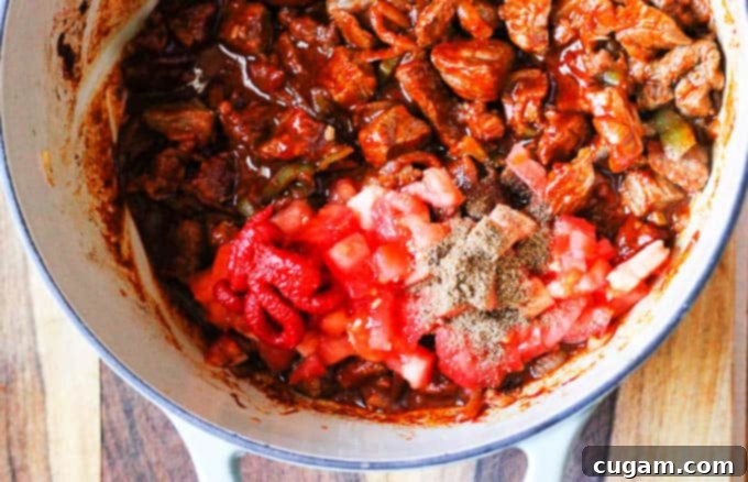 Mixing in tomatoes and tomato paste with beef and paprika