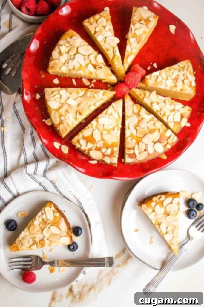 Zesty Gluten Free Lemon Cake 2 Red cake pedestal with lemon cake topped with sliced almonds. Cake is cut into pieces and there are two plates with slices of cakes plus a few berries.