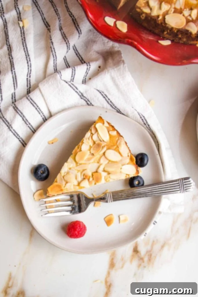 Zesty Gluten Free Lemon Cake 14 Slice of lemon cake with almonds and a few berries on a small white plate, with a fork.