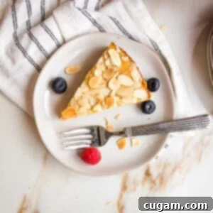 Zesty Gluten Free Lemon Cake 17 small white plate with slice of lemon cake topped with sliced almonds. Plate has a few blueberries, a raspberry and some almond slices.