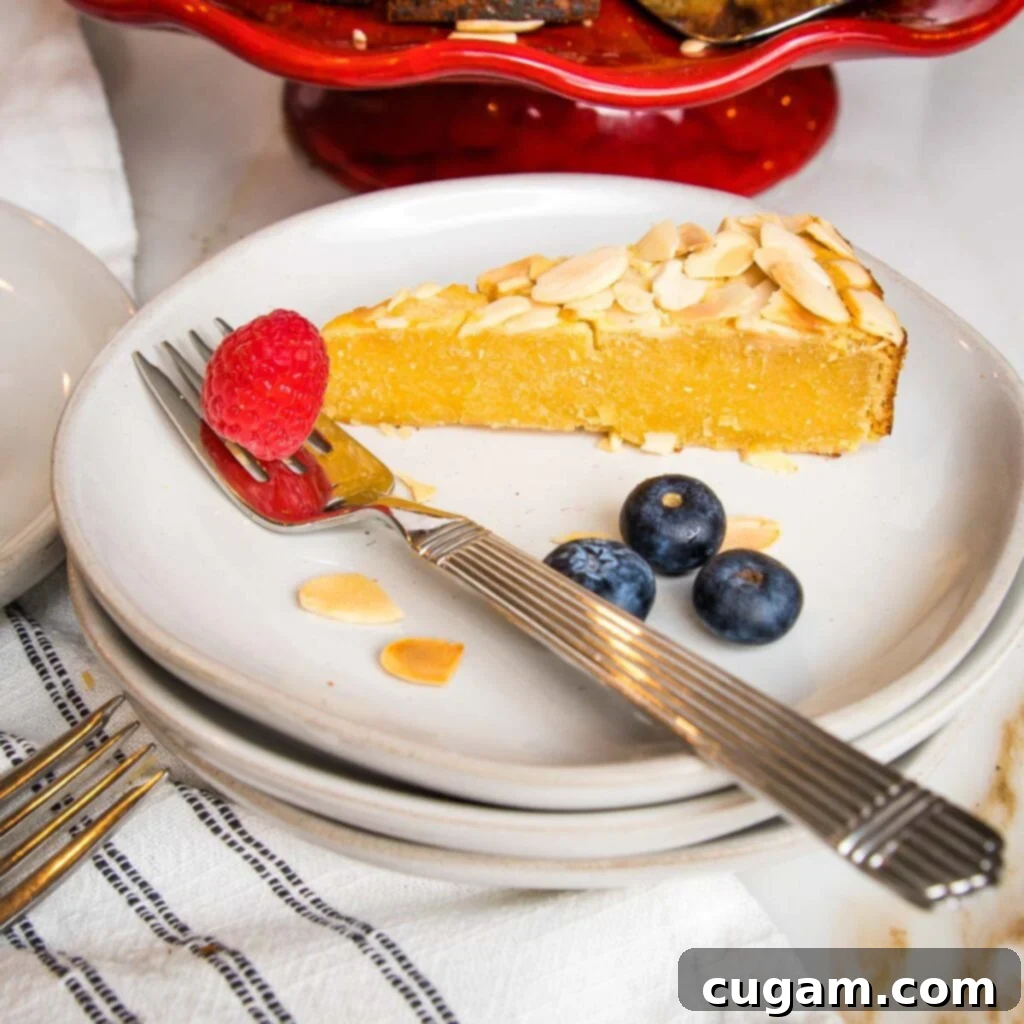 Zesty Gluten Free Lemon Cake 4 Side view of a piece of lemon cake on a white rimmed plate with a few blueberries and a raspberry plus a few sliced almonds on the plate.