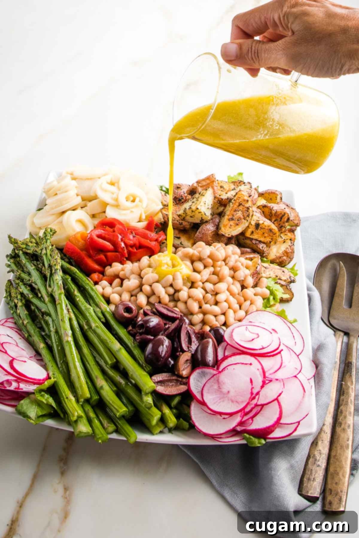 Lemon Vinaigrette being poured over a vegan nicoise salad in colorful sections on a large white platter.