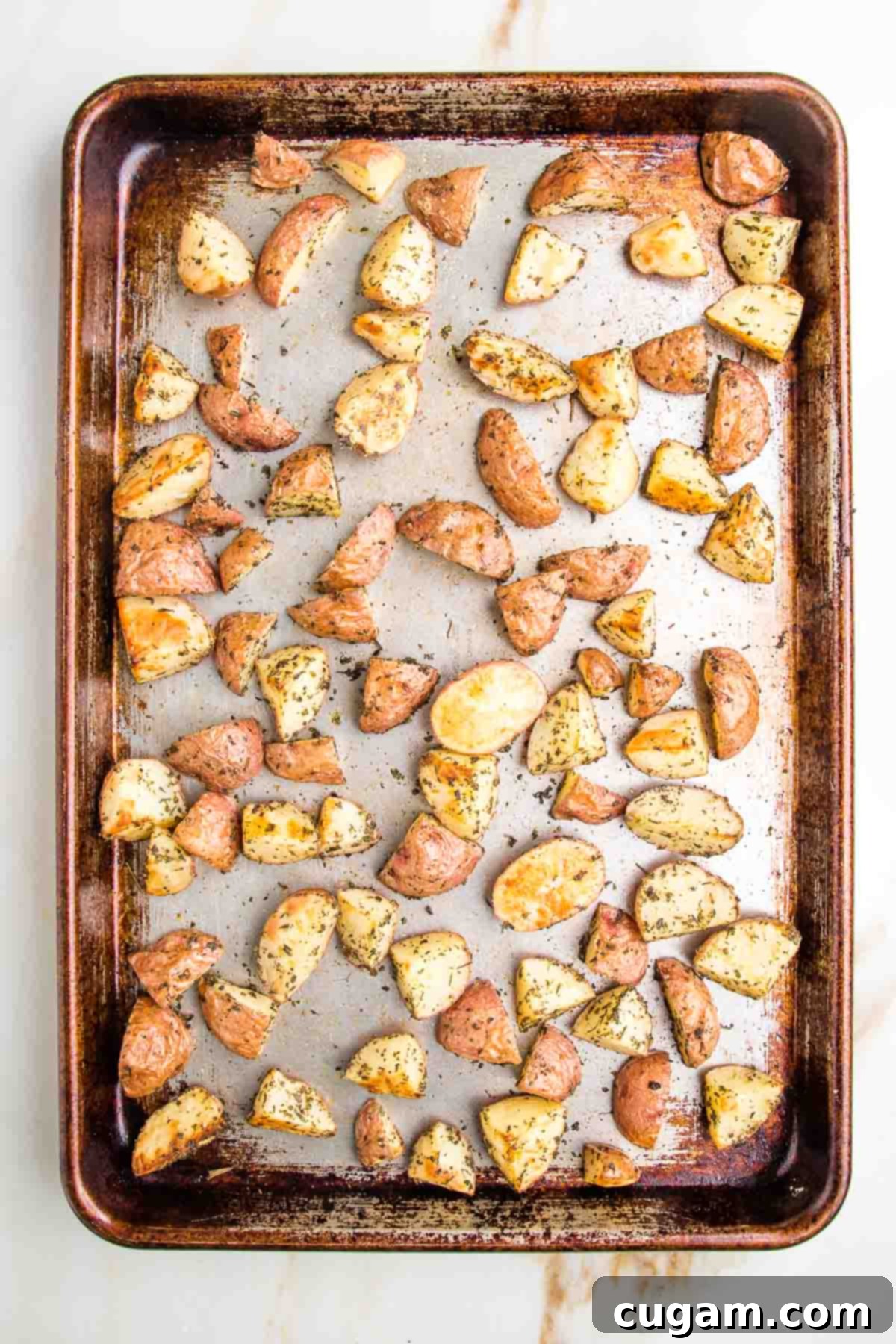 rimmed baking tray with potatoes cut into halves and quarters, roasted with herbs
