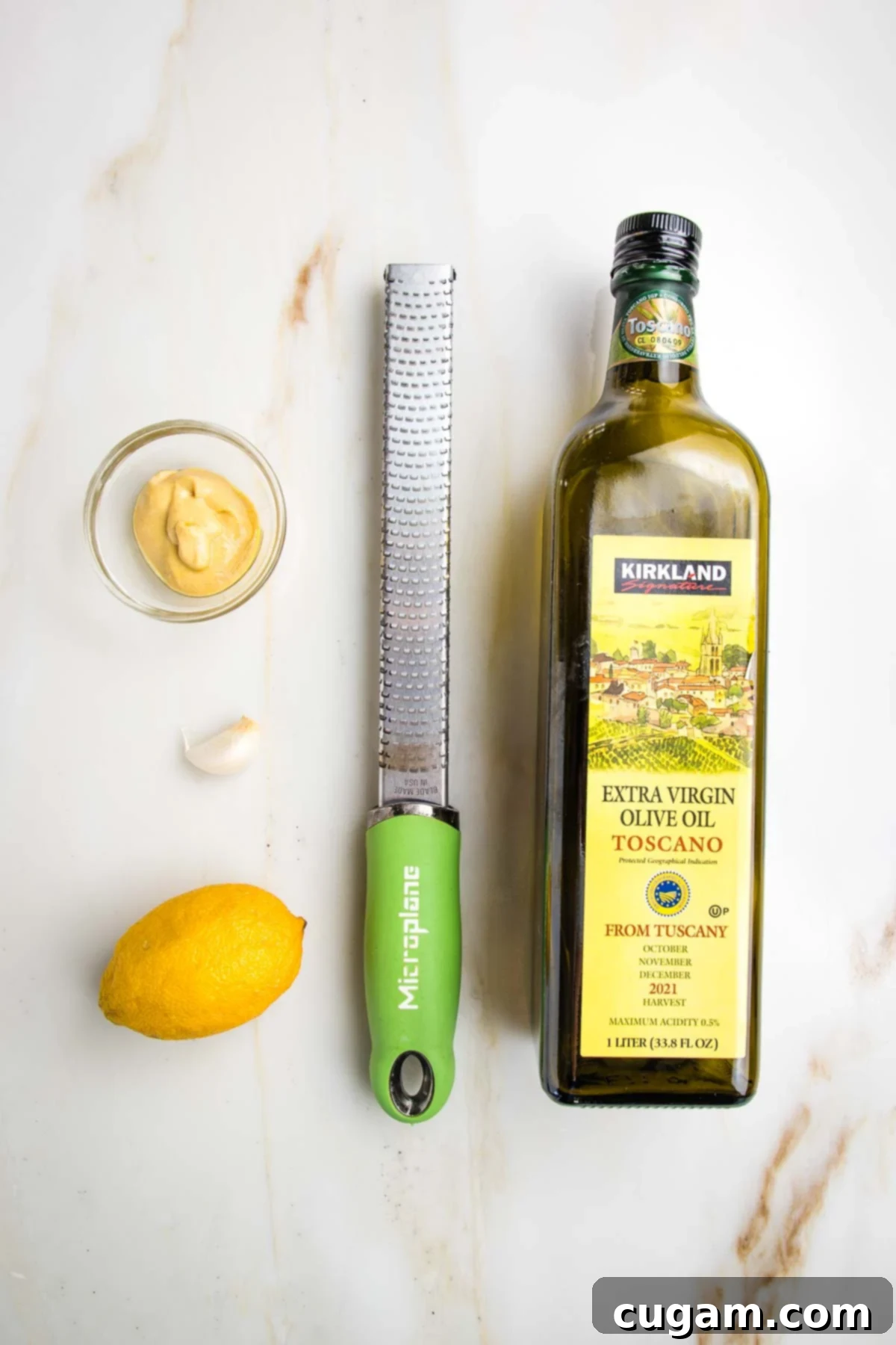 Ingredients for nicoise salad dressing: olive oil, dijon mustard, lemon and garlic shown with a microplane zester.