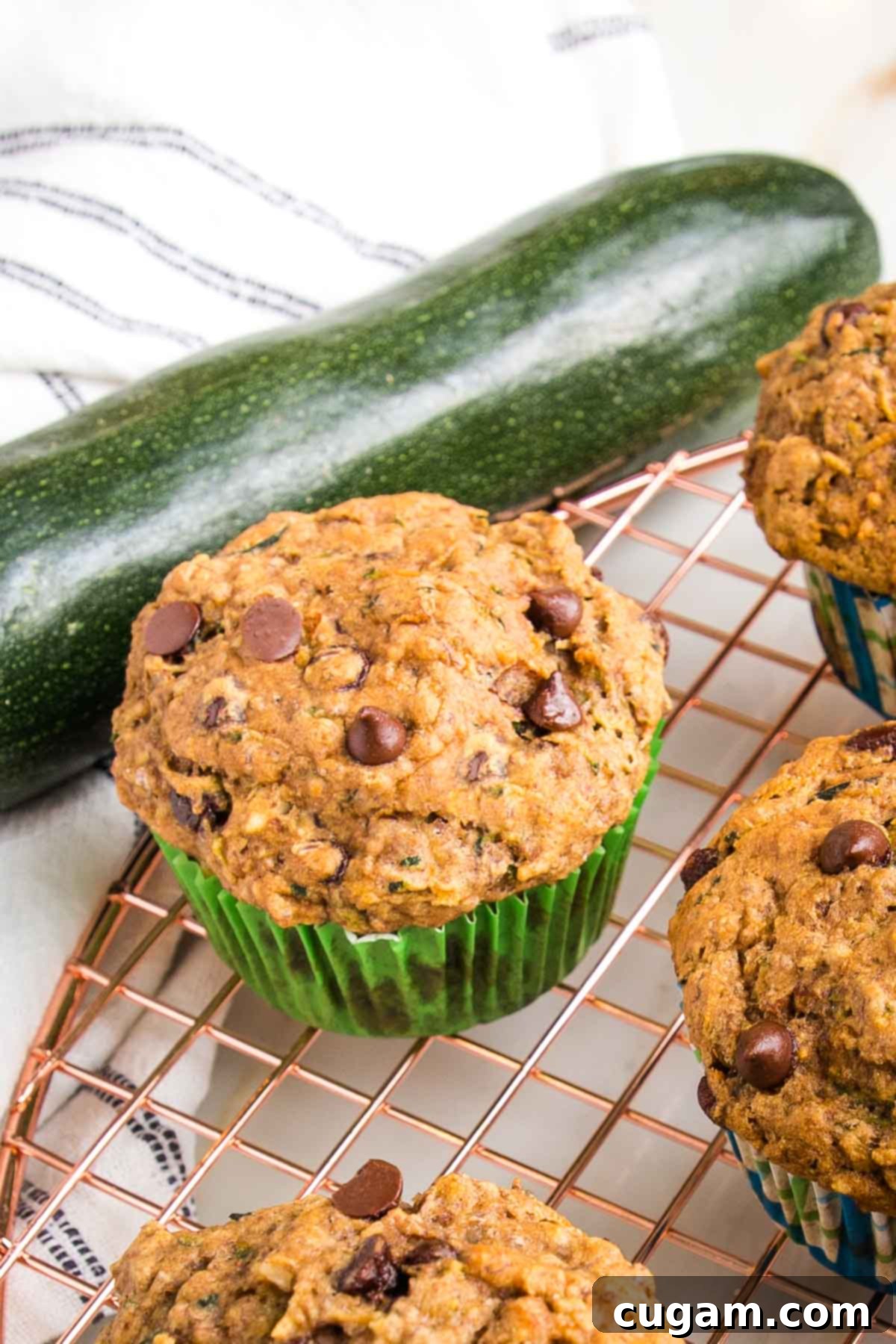 Vegan Zucchini Muffins 2 Chocolate chip zucchini muffin, cooling on a wire rack, with a large fresh zucchini in the background, hinting at the key ingredient.