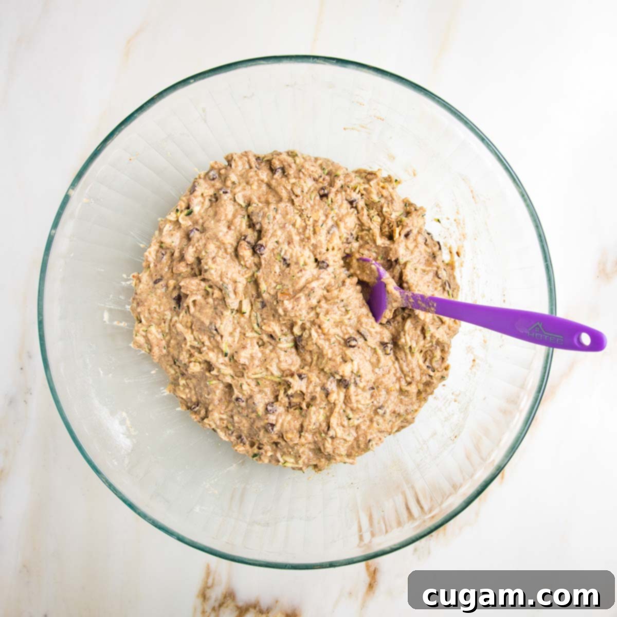 Vegan Zucchini Muffins 12 Light brown zucchini muffin batter. You can see mini chocolate chips and the shredded zucchini and some chopped nuts, perfectly mixed and ready for baking.