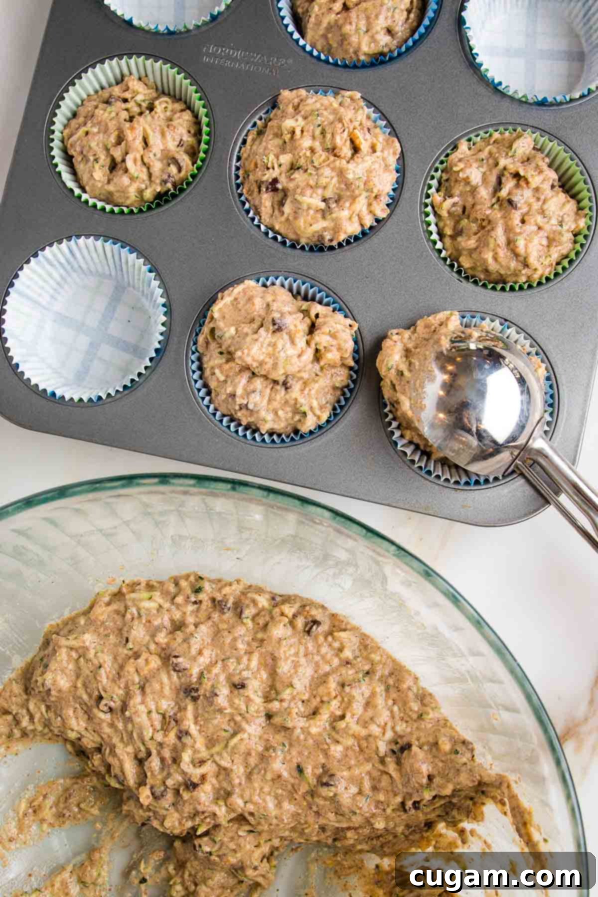 Vegan Zucchini Muffins 13 Zucchini muffin batter in a large mixing bowl. Cookie scoop portioning batter into muffin tin lined with parchment paper liners, ensuring even distribution.