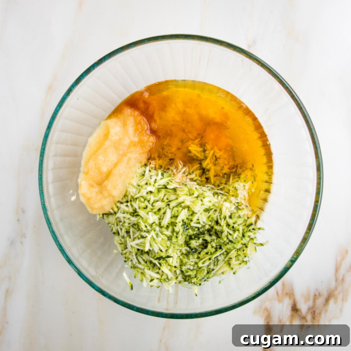 Vegan Zucchini Muffins 5 Wet ingredients for zucchini muffins. In a large glass bowl: applesauce, shredded zucchini, honey, vanilla and mashed banana, ready to be mixed for a healthy batter.