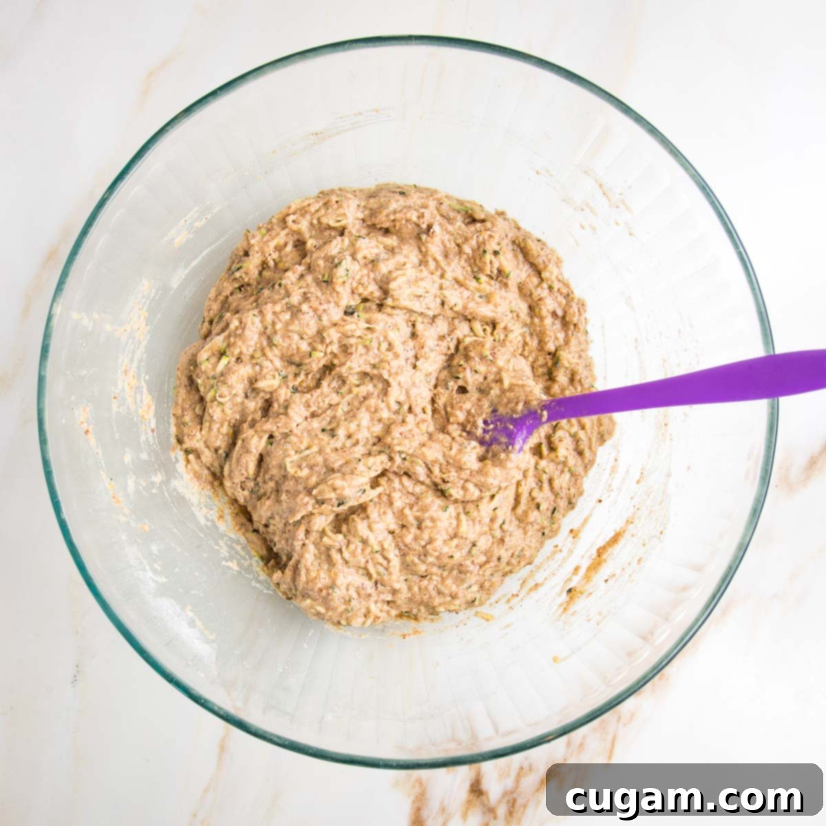 Vegan Zucchini Muffins 10 Large glass mixing bowl with lumpy zucchini muffin batter and a purple spatula, showing the perfect consistency before adding mix-ins.