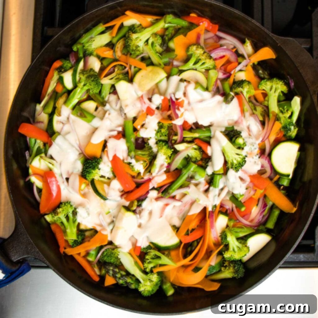 Cast iron skillet with colorful sauteed vegetables topped with a swirl of creamy primavera sauce.