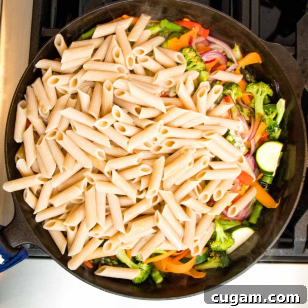 Cast iron skillet filled with colorful sauteed vegetables and topped with just cooked penne pasta. 