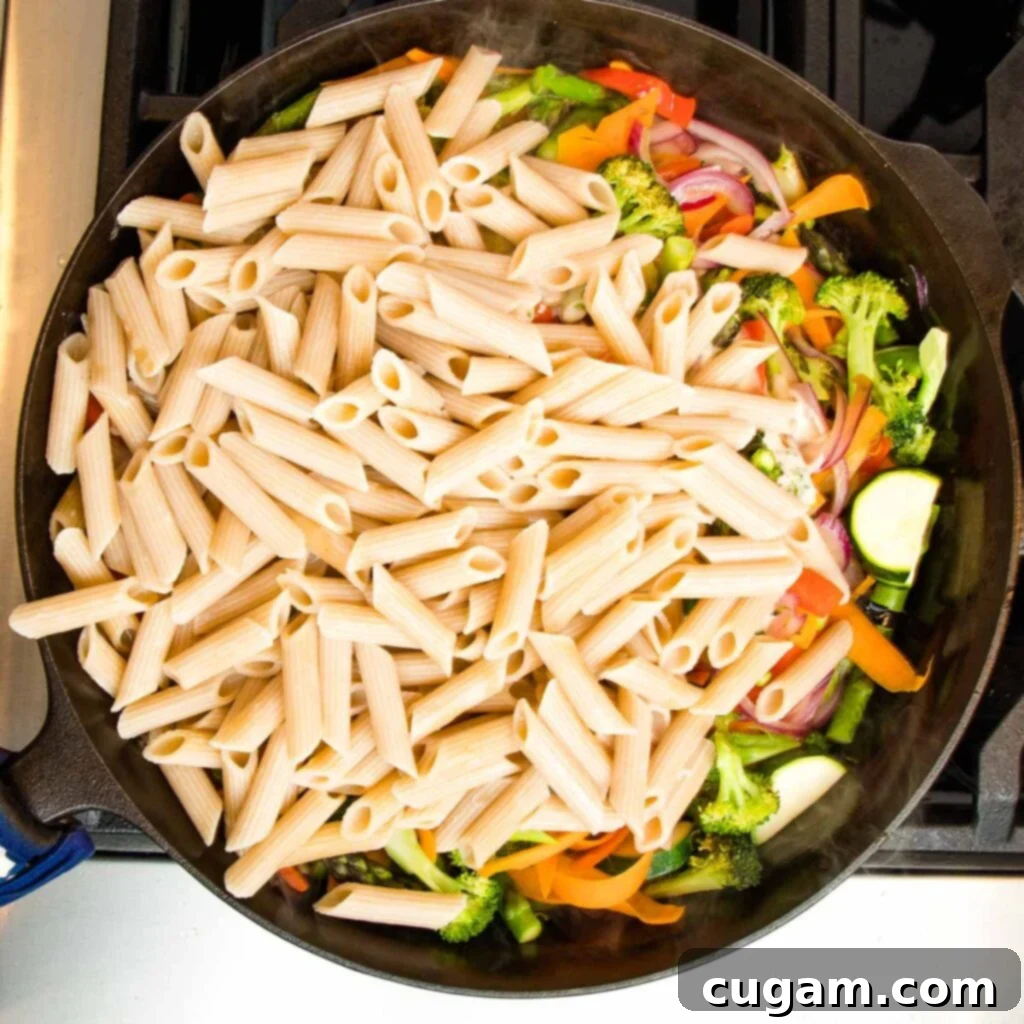 Cast iron skillet filled with colorful sauteed vegetables and topped with just cooked penne pasta. 