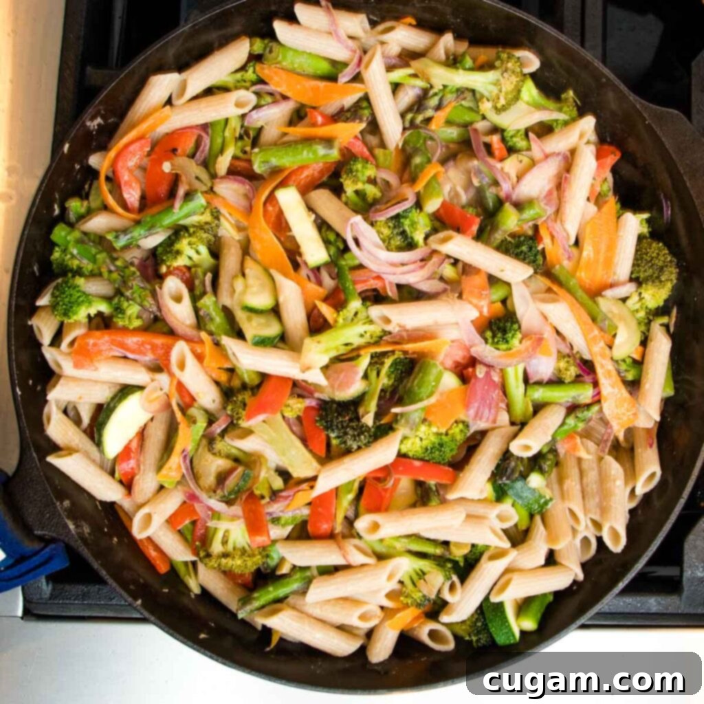Pasta and vegetables being tossed together.
