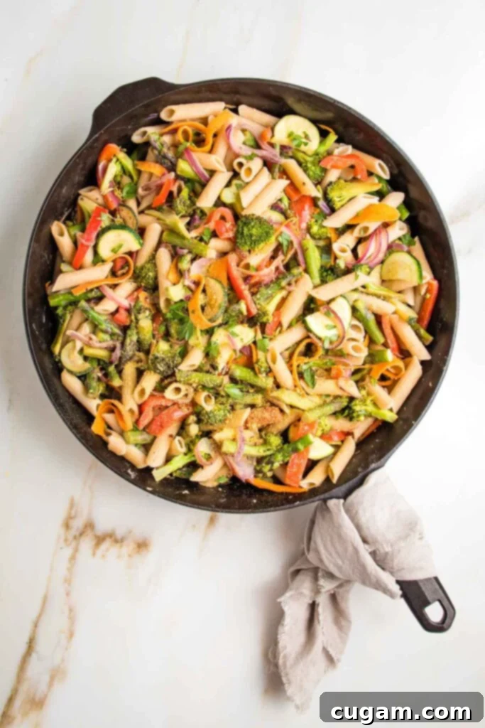 Cast iron skillet, with linen napkin on handle, filled with colorful veggies and pasta. 