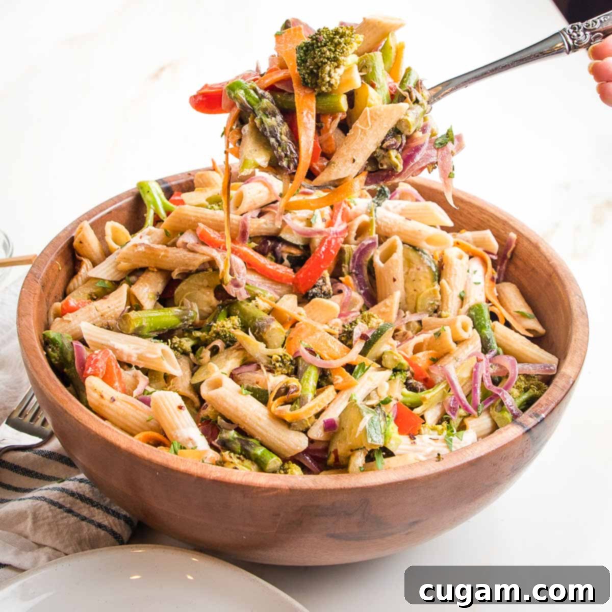 Two hands holding small bowls of vegan pasta primavera, showing the vibrant mix of pasta and vegetables.
