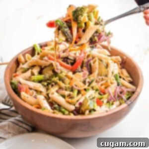 wooden bowl filled with penne pasta and lots of colorful veggies. There is a large spoon scooping up a bunch to plate.