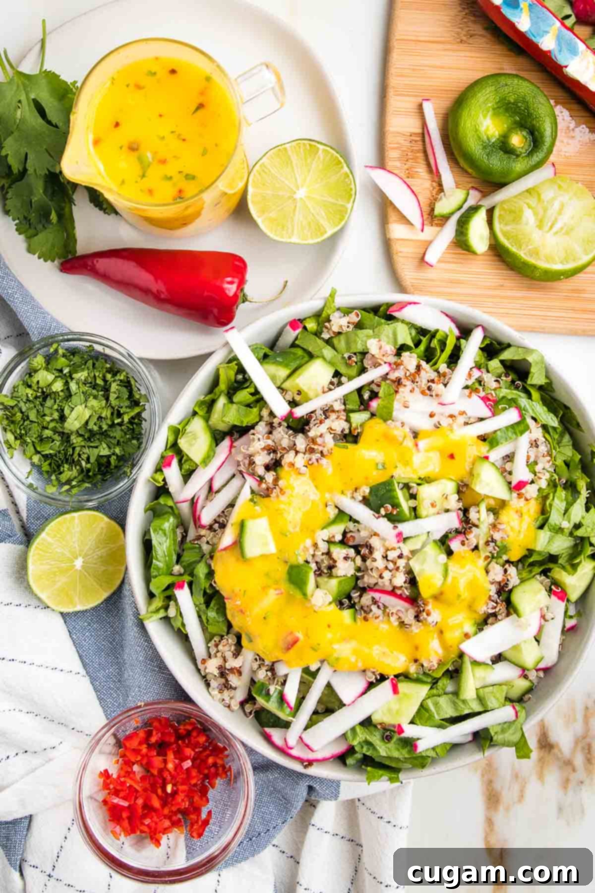 Bright yellow mango salad dressing in a glass pitcher, a bowl of simple salad with same yellow dressing, lots of colorful chopped veggies strewn about.