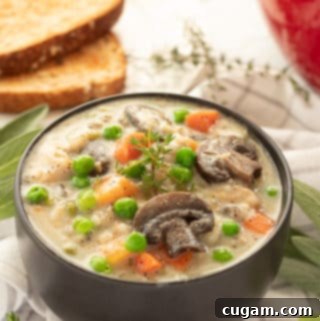 A ceramic bowl filled with creamy chicken wild rice soup, garnished with fresh herbs and a spoon, sits on a rustic wooden surface.