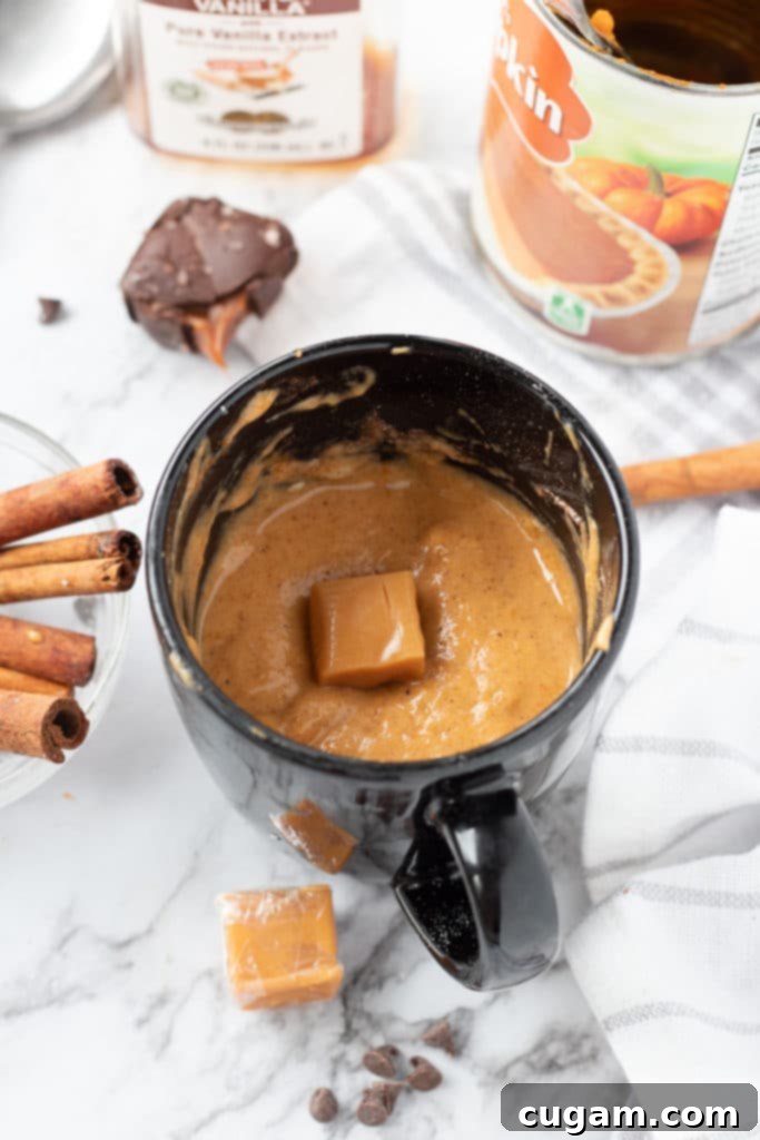 Raw pumpkin mug cake batter in a mug with a soft caramel pressed into the surface, ready for microwaving.