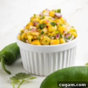 Vibrant Pineapple Mango Salsa 8 Side view of a small white bowl piled high with pineapple mango salsa. Bright yellow fruit with chunks, purple onion, green flecks of cilantro and jalapeno.