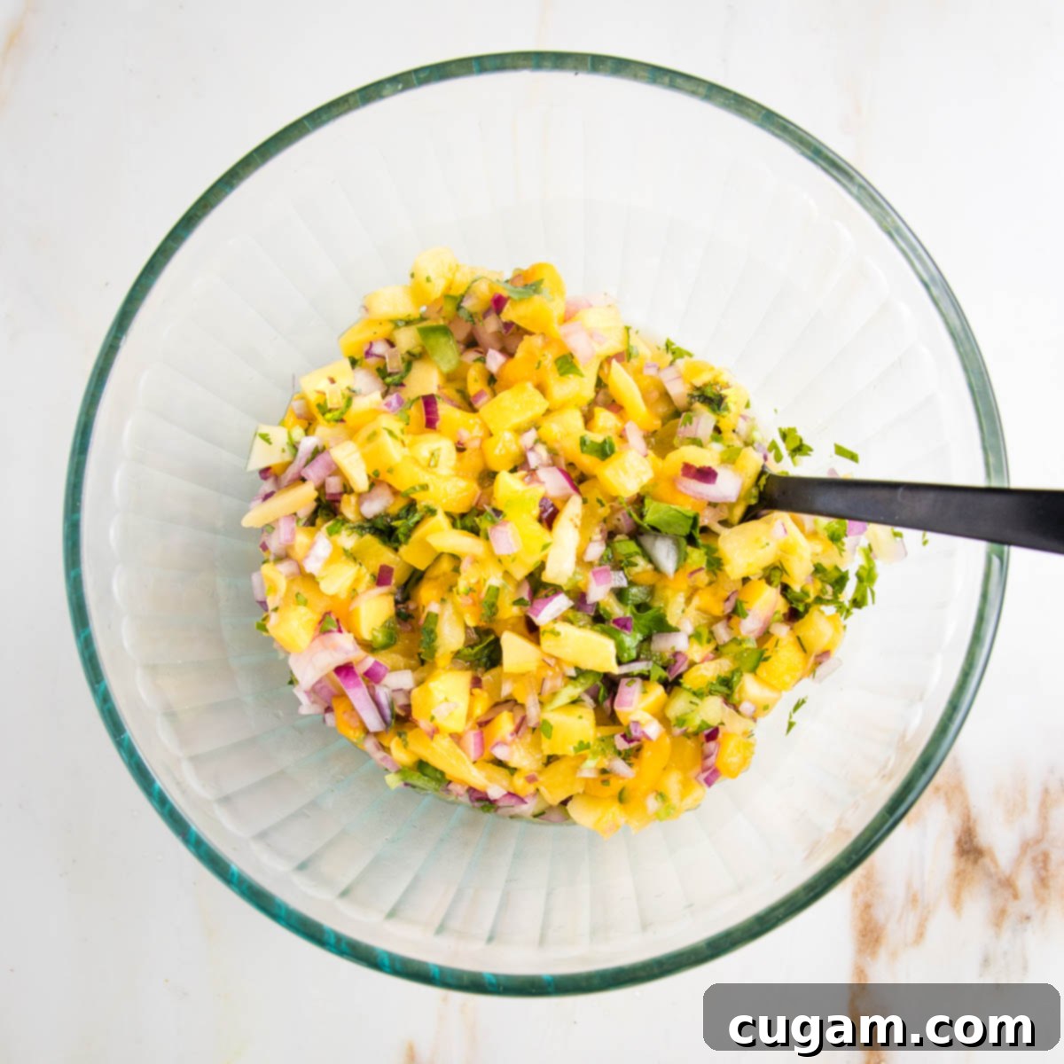 Vibrant Pineapple Mango Salsa 5 Glass bowl with colorful fruit salsa and a large spoon. Salsa is yellow from mango and pineapple, purple onions, green jalapenos and green cilantro.