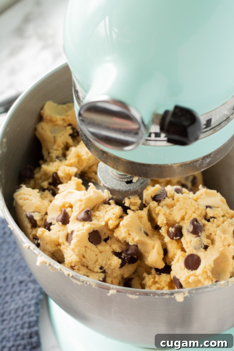 Raw chocolate chip pudding cookie dough being mixed in a blue stand mixer, showing its soft texture.