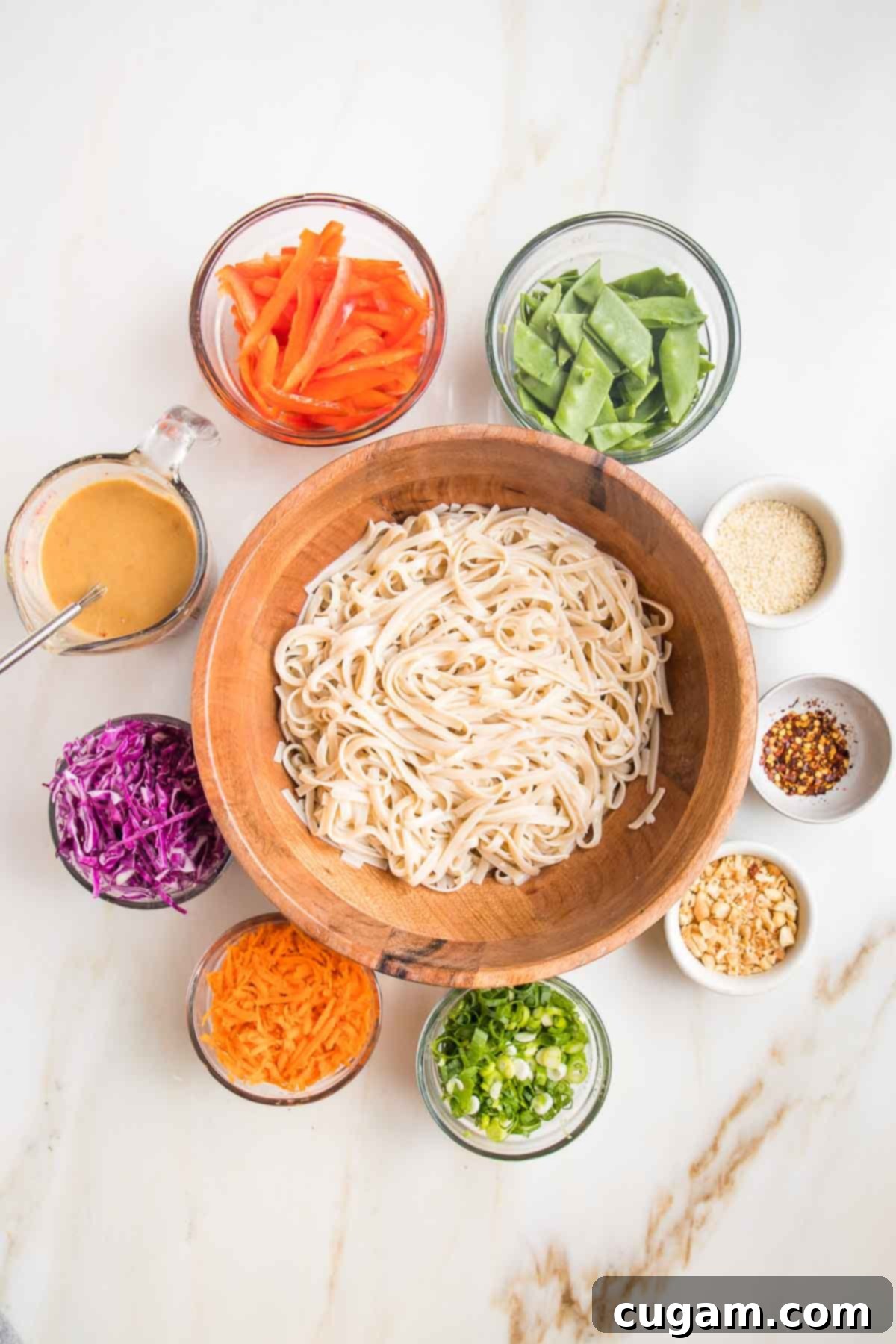 Wooden bowl with cooked rice noodles. Small bowls around with brightly colored sliced vegetables. 