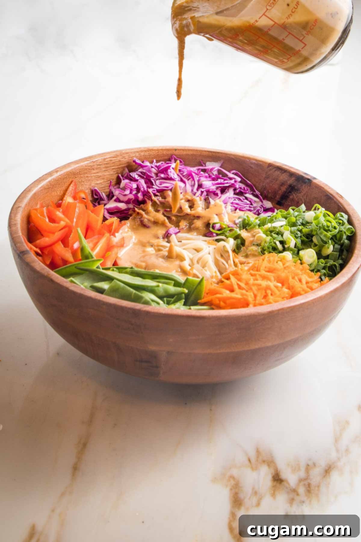  Tahini sauce pouring over the center of wooden bowl with sections of brightly colored veggies.