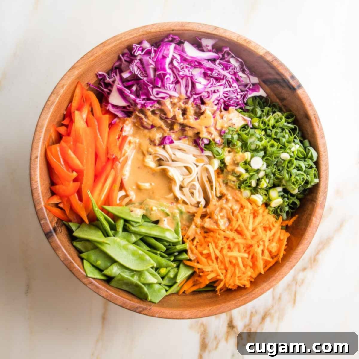 Large bowl of sectioned brightly colored veggies and noodles with tahini sauce in the center. 