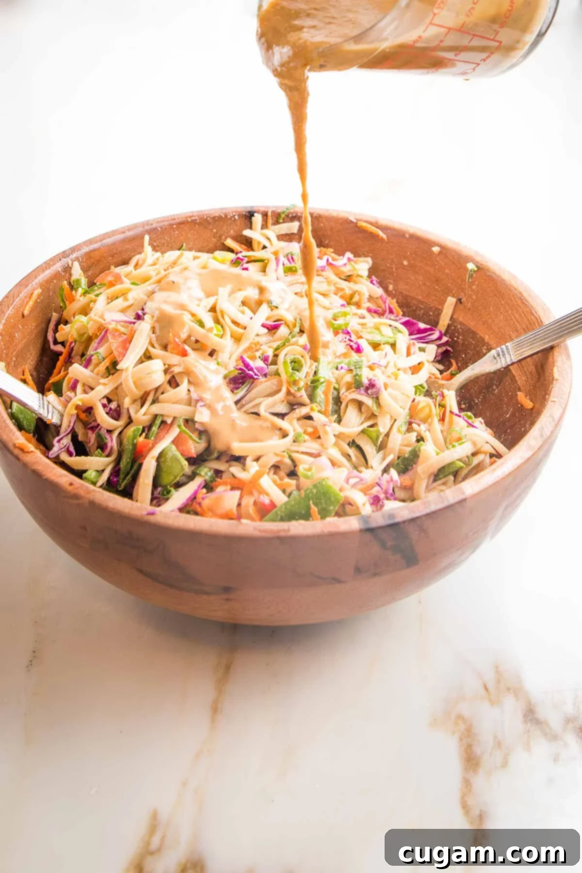 Sesame sauce poured over noodles and veggies in a wooden bowl.  