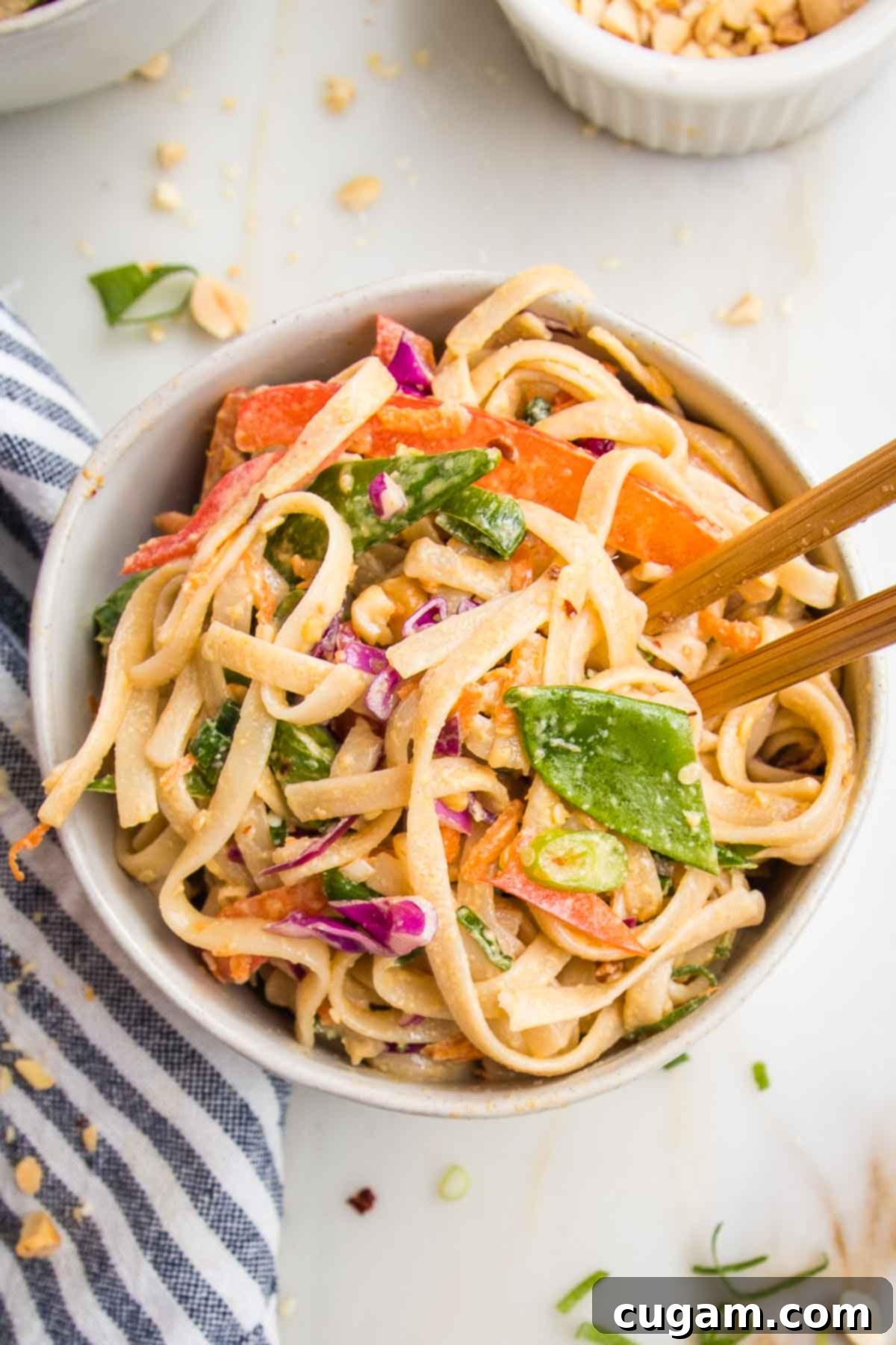 Small white bowl filled with pad thai noodles and crunchy bright veggies, tossed in a spicy tahini sauce. 