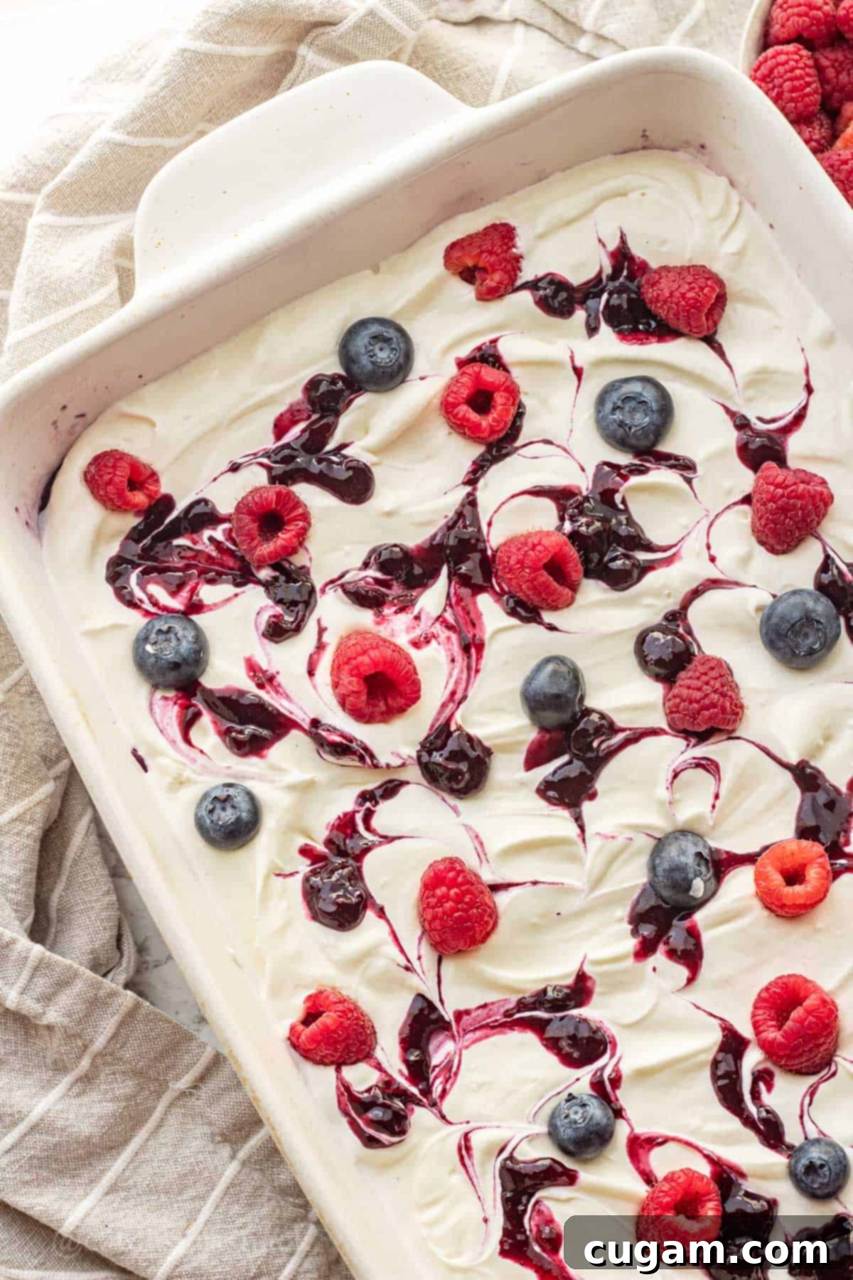 Blueberries and raspberries on whipped filling and blueberry jello in white dish.