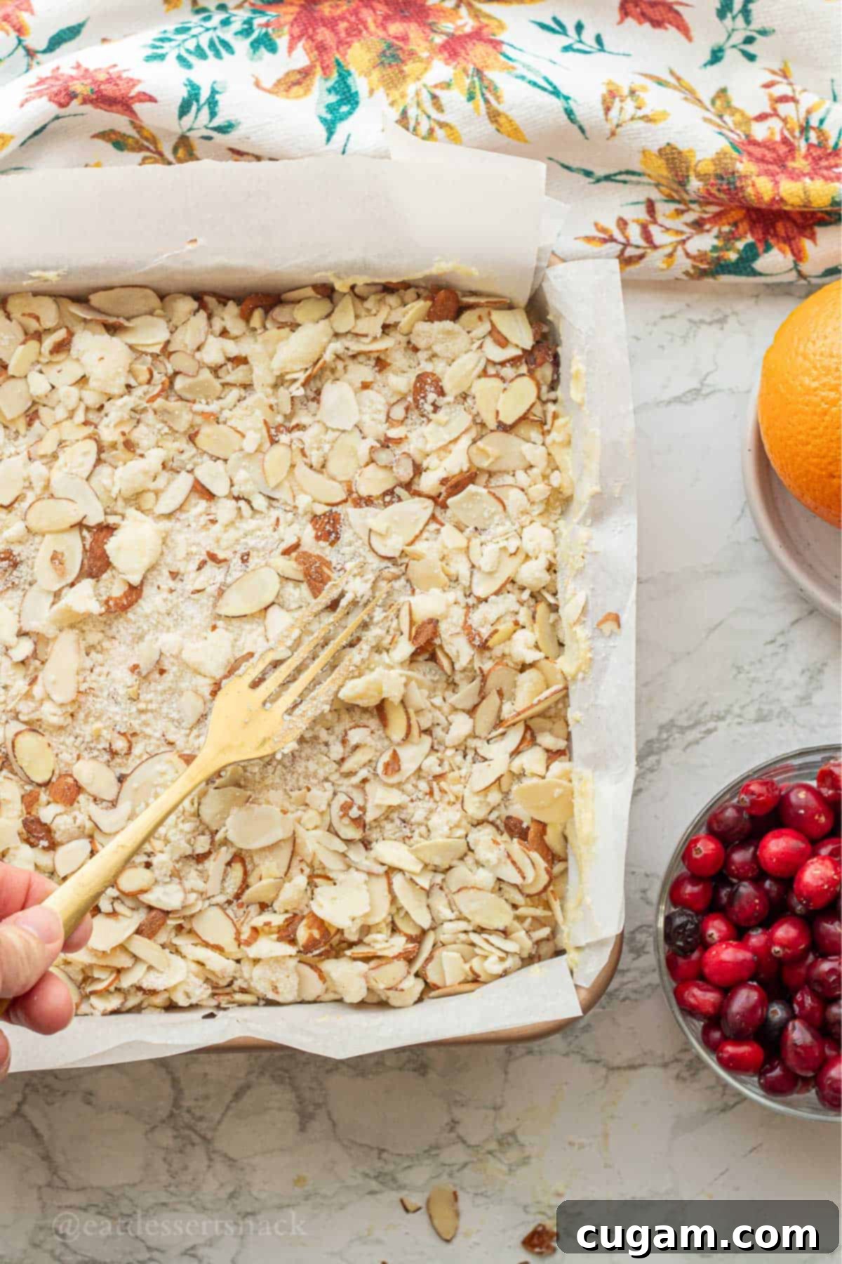 Almond streusel mixture being spread evenly over the raw cranberry orange cake batter in a baking pan.