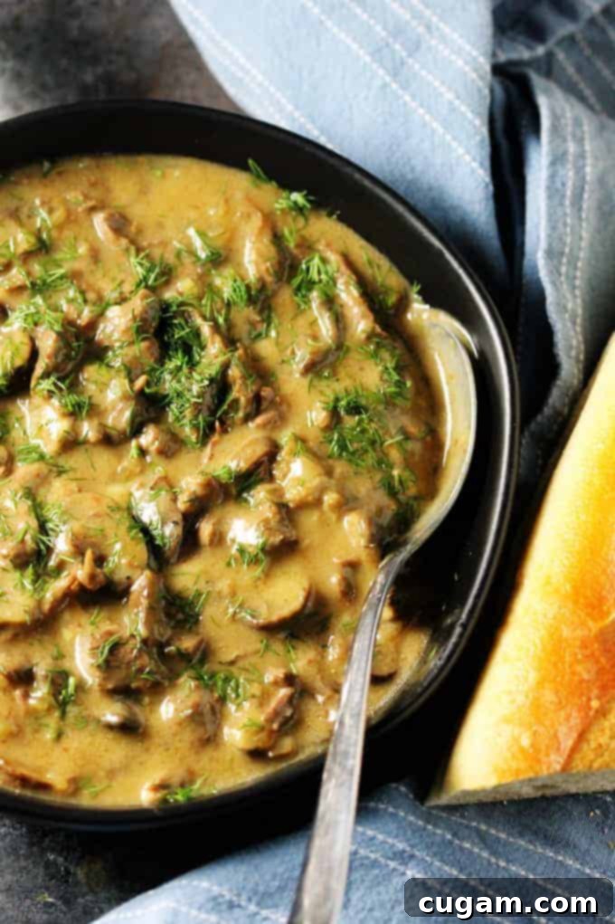 Close up shot of a black bowl filled with creamy beef stroganoff, showing tender beef and mushrooms