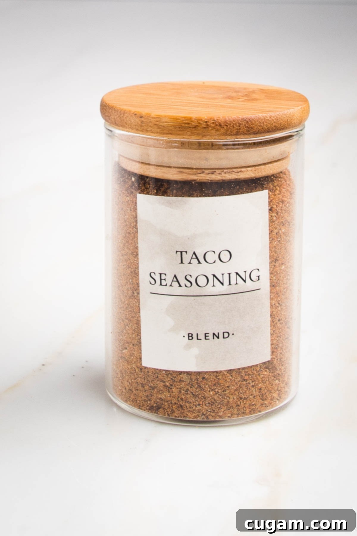 Small spice jar with wooden lid labeled "taco seasoning-blend" with a orangy-rust colored powder inside. 