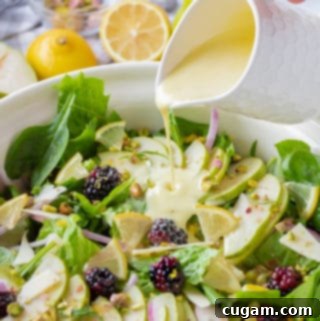 Salad dressing drizzling over blue bowl of blackberry pear salad.
