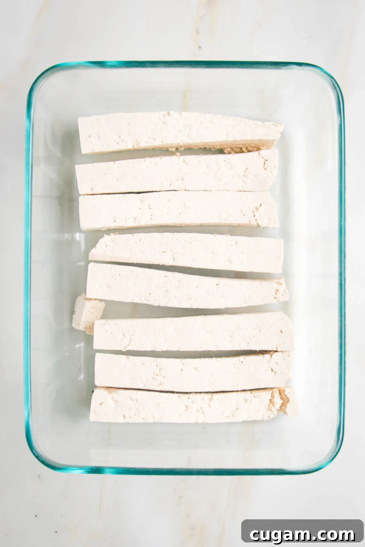 Long, thin slices of tofu for satay in a rectangular glass dish.