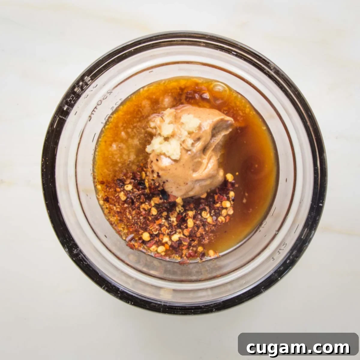 Small glass bowl with peanut butter, tamari, other liquid and some crushed red pepper visible.