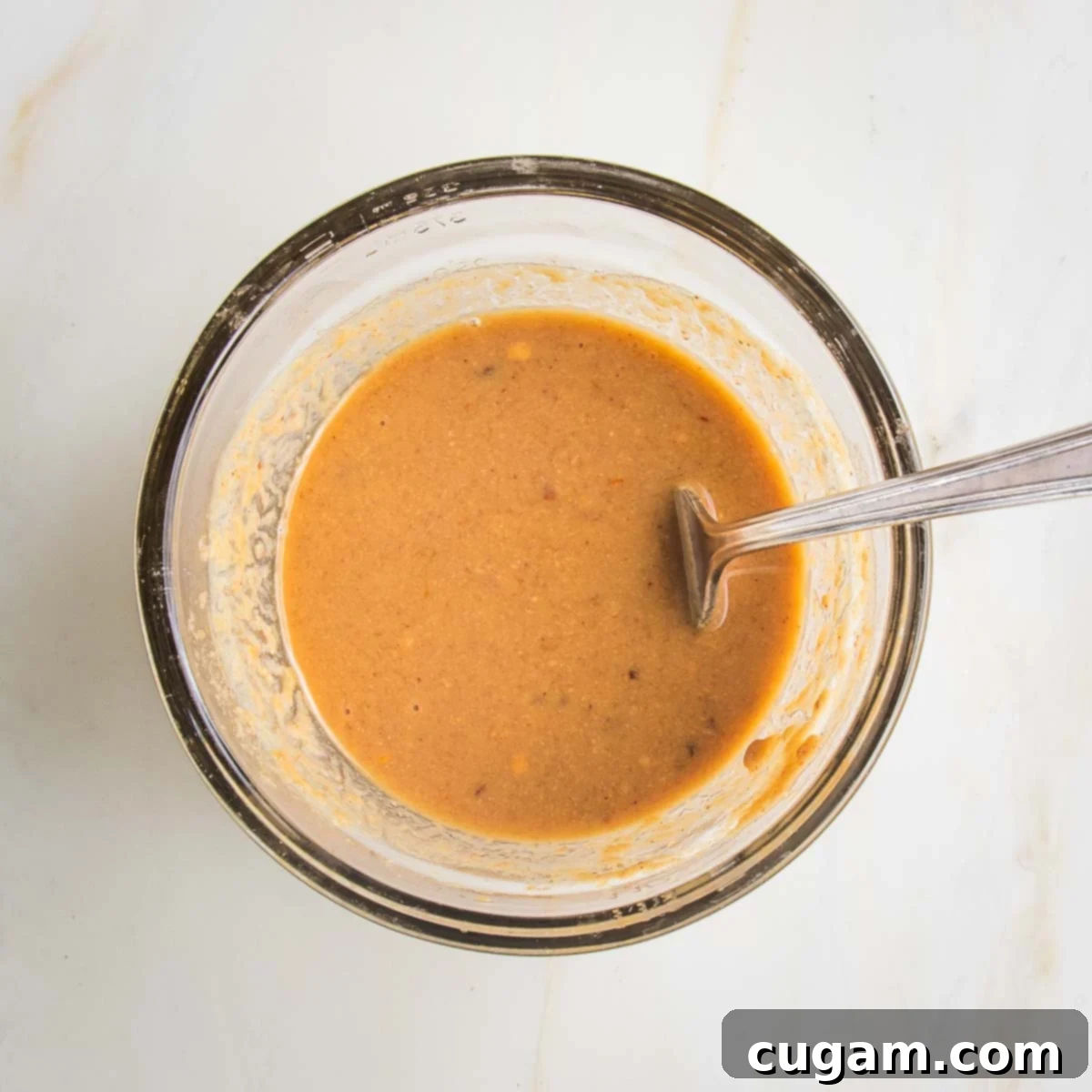 Small glass bowl with fork that's mixed together an orangy-brown peanut butter sauce.