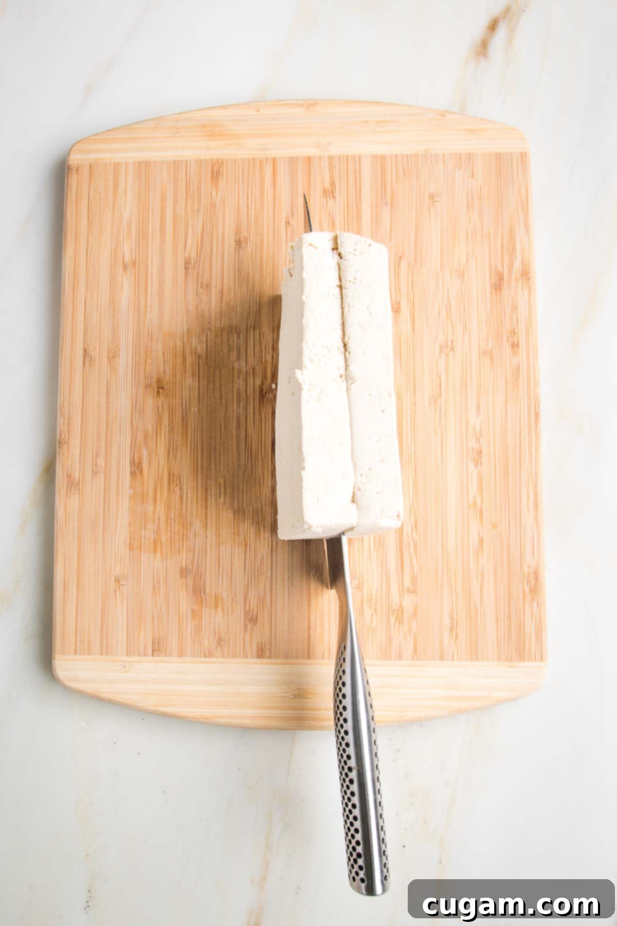 Slicing through a block of tofu, on a wooden cutting board.
