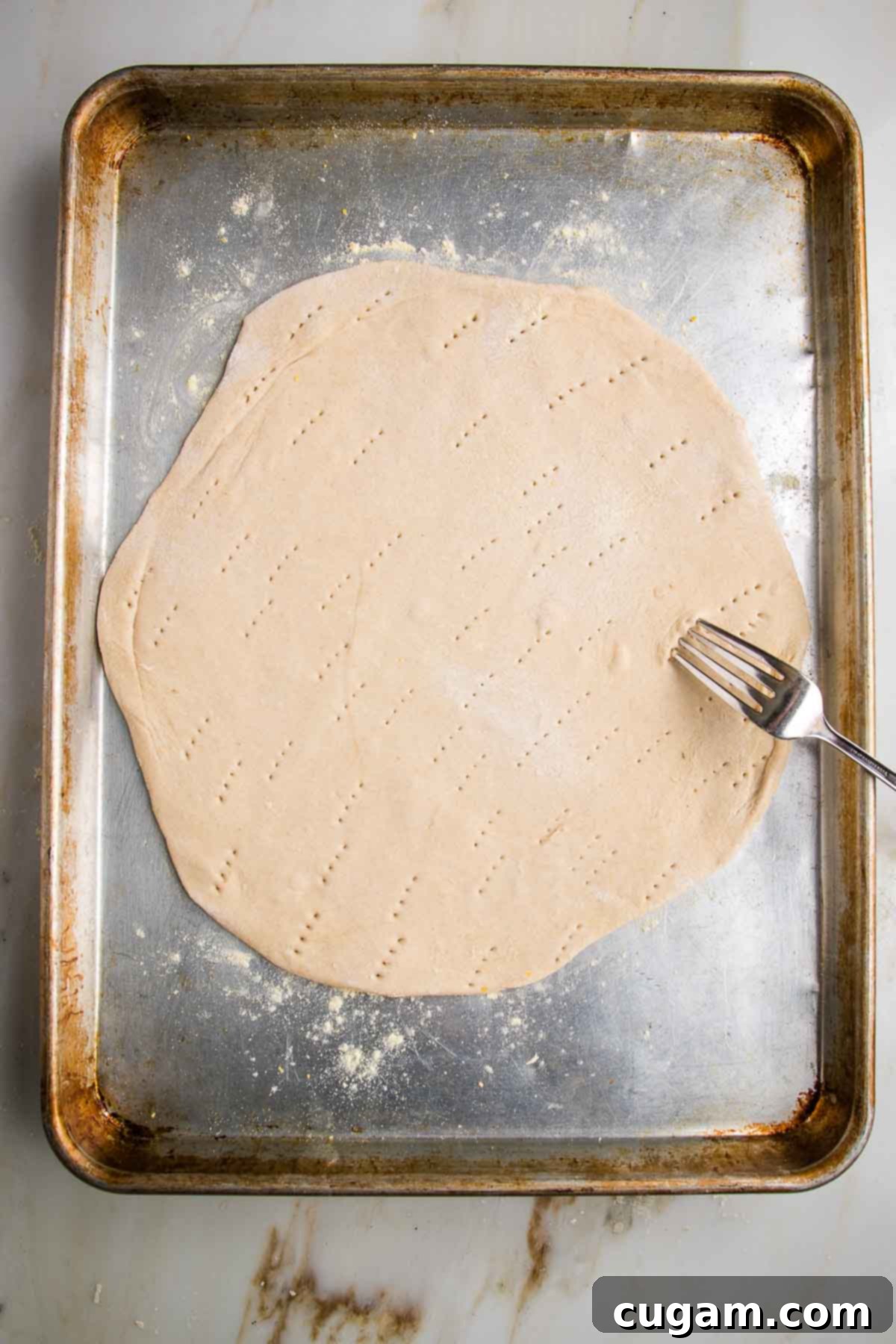 Flatbread pizza dough, rolled out and placed on baking sheet. A fork is pricking holes throughout.