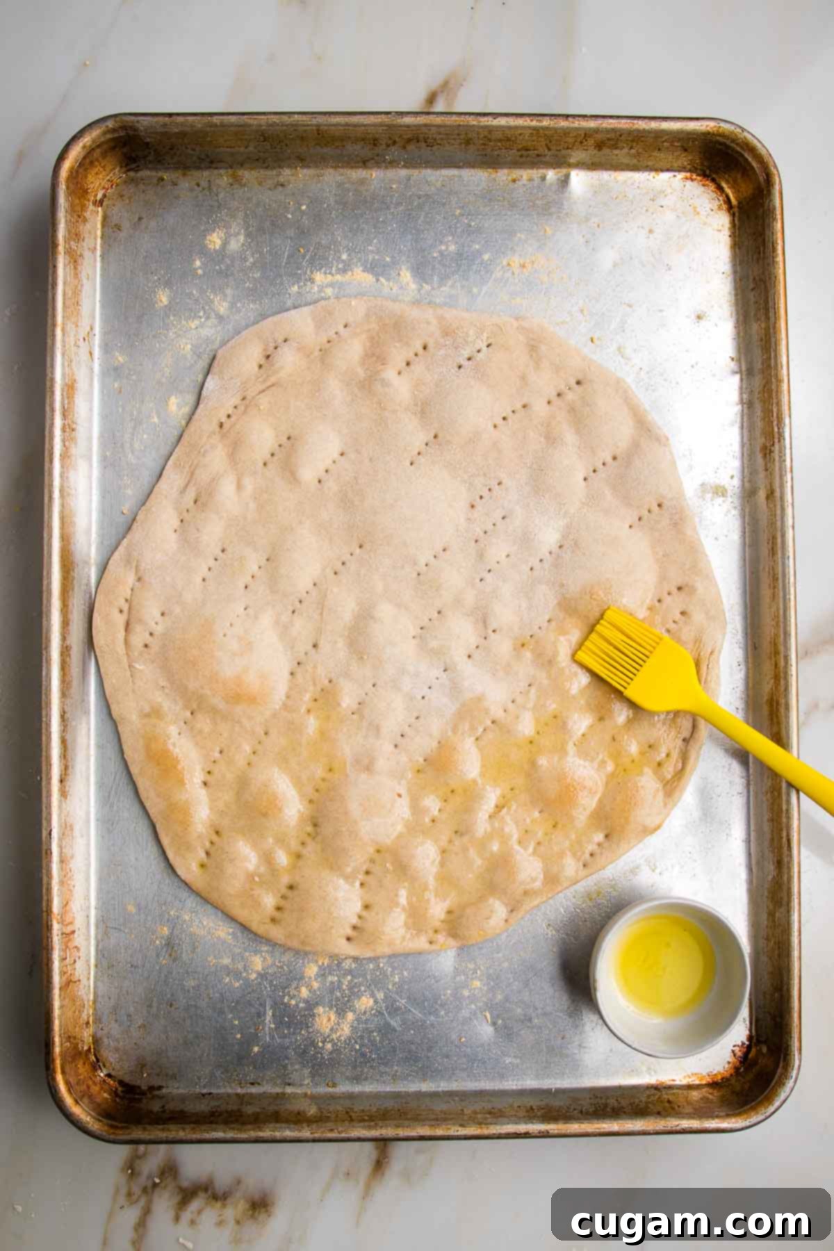 Flatbread pizza dough, partially cooked and being brushed with olive oil.
