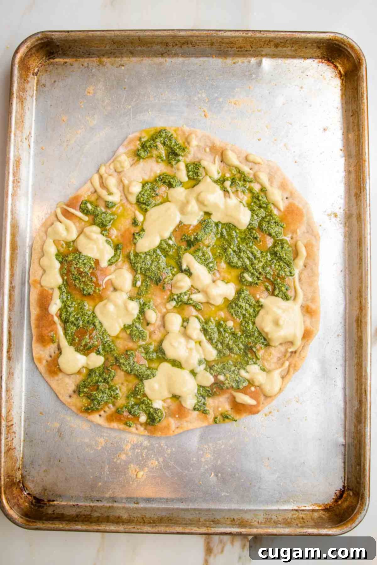 Flatbread pizza dough with dollops of hummus and pesto on top.