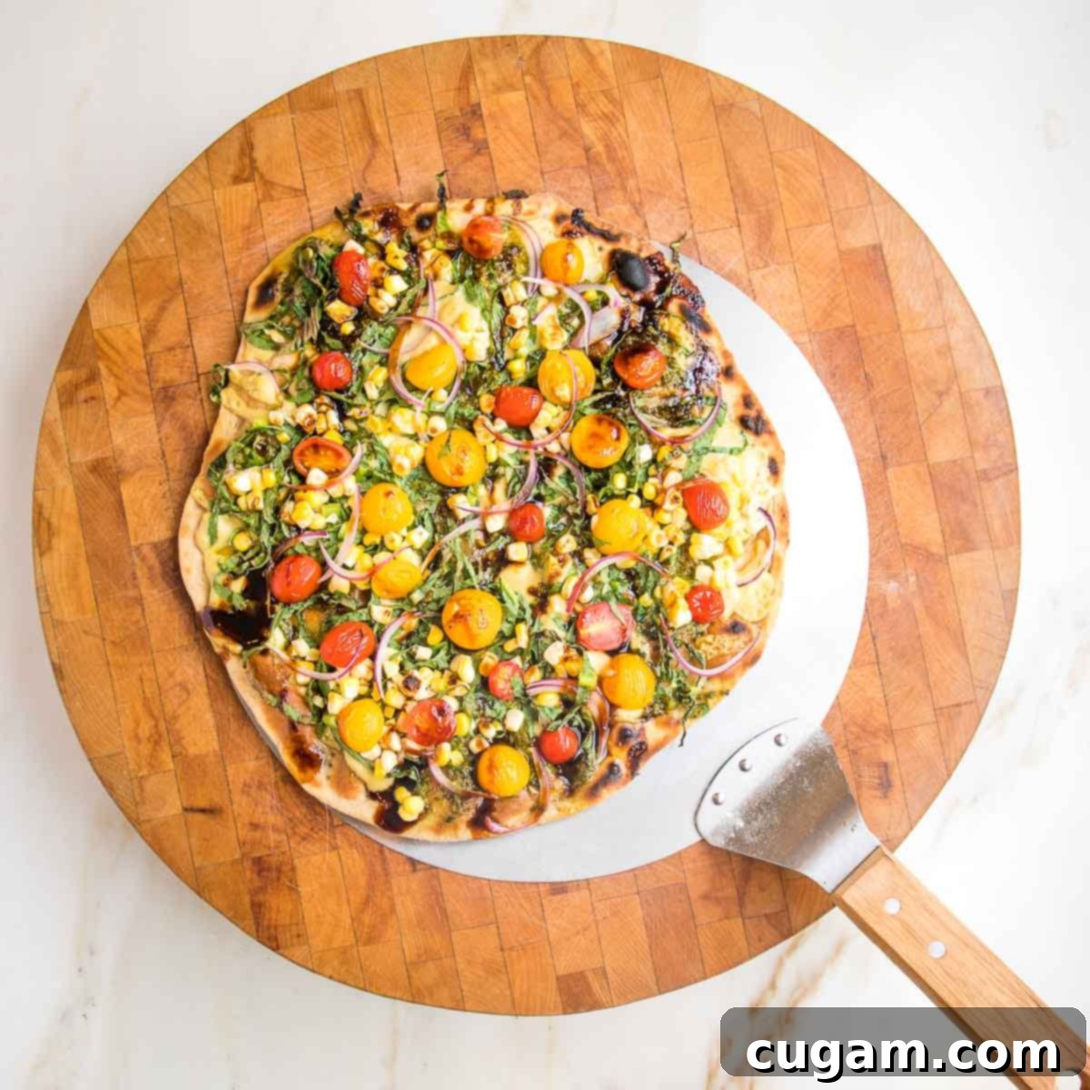 Pizza peel delivering flatbread with colorful toppings onto a wooden cutting board.