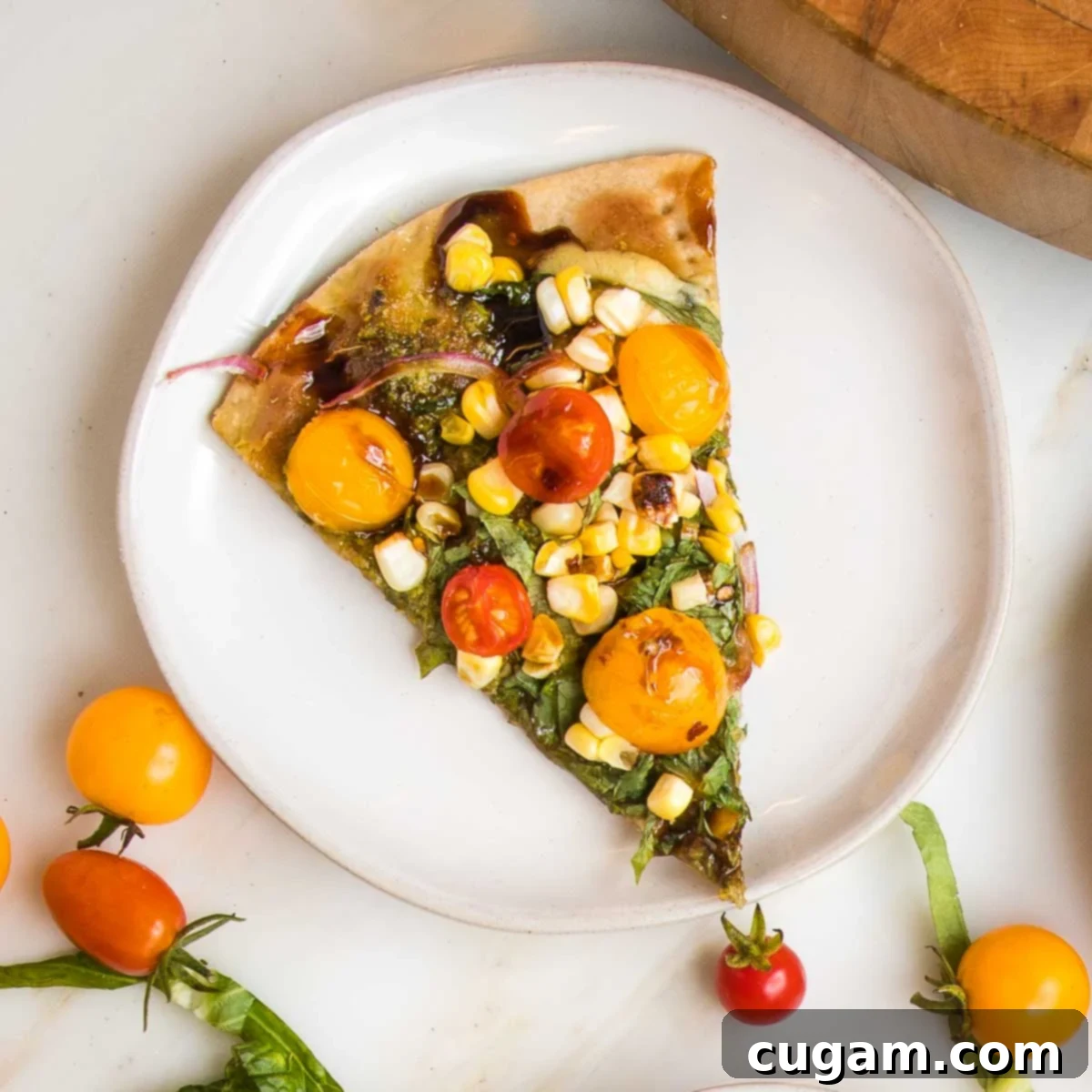 Slice of flatbread topped with tomatoes, corn, onions and basil on a small white rimmed white. 